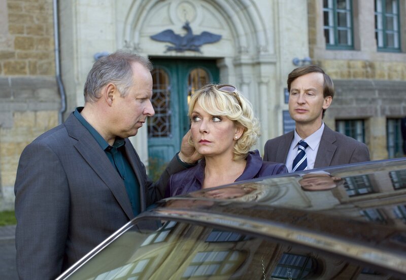 Hannes (Axel Milberg, li.) versucht seine reiche Geliebte Anette (Janette Rauch) zur Einstellung eines Bodyguards zu überreden, skeptisch beäugt von ihrem Privatsekretär Dr. Bittins (Jan Henrik Stahlberg). – Bild: ZDF/​ARD Degeto/​Thorsten Jander