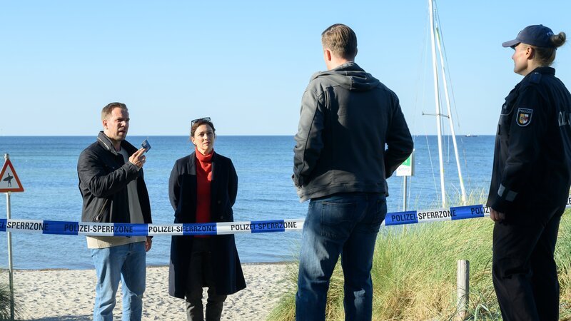 Der ermordete Kitesurfer war hauptberuflich bei einer Reederei angestellt und hat während der Surf-Saison zusätzlich in der Kiteschule von Bastian Kuhnstein (Matthias Reichwald, 2.v.r.) unterrichtet. Lars Pöhlmann (Dominic Boeer, l.) und Karoline Joost (Nike Fuhrmann, 2.v.l.) wollen wissen, ob die berufliche Mehrfachbelastung private Konflikte verursacht hat. – Bild: ZDF /​ Meyerbröker