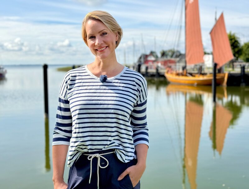 In Ahrenshoop steigt Judith auf eines der typischen Zeesboote mit ihren braunen Segeln. – Bild: WDR/​Bavaria