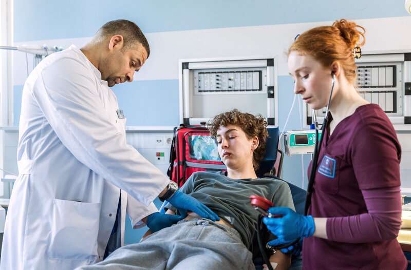 Dr. Matteo Moreau (Mike Adler, l.) und Assistenzärztin Tamar Hummel (Linda Kummer, r.) untersuchen El Fabeck (Antonia Baumgartner, M.) und stellen Prellmarken über den Rippen fest. Hat El innere Verletzungen? – Bild: ARD/​Michael Kremer