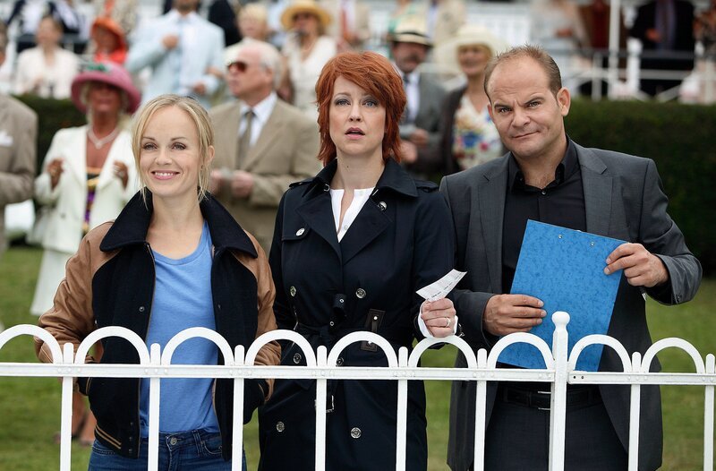 Gespannt verfolgen Nadja Bock (Floriane Daniel, M.),  Johannes Sonntag (Matthias Klimsa, r.) und Julia Klug (Friederike Kempter, l.) den Start des Hauptrennens auf der Galopprennbahn Berlin-Hoppegarten. Die Chefin hat auf den hohen Favoriten „Chardonnay“ gesetzt. – Bild: NDR/​ARD/​Daniela Incoronato