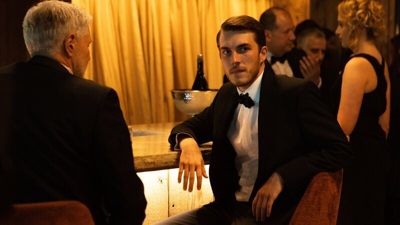 Aaron (Felix Mayr, M.) nimmt mit Hintergedanken an einem Empfang seines Vaters in London teil. – Bild: ZDF und Nicolas Velter – A&ENetworks