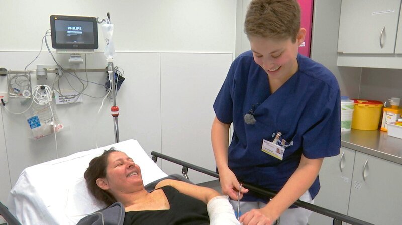 Die Patientin Sylvia Treusch (liegend) hat sich den Arm gebrochen. Krankenschwester Clara Henneberger aus der Notaufnahme der BGU Frankfurt versorgt sie. – Bild: HR