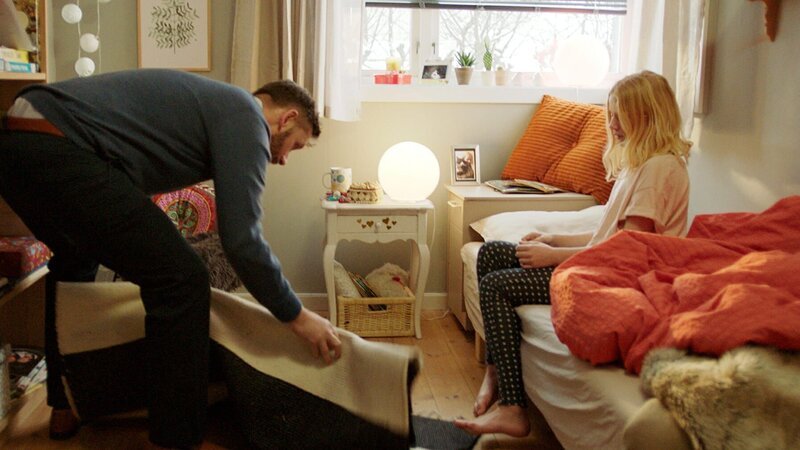 Sannes Vater (Jan Martin Johnsen, l.) entfernt den Teppich, um Sanne (Tilde Ender Søvik) das Aufstehen zu erleichtern. Denn die Streifen des Teppichs veranlassen Sanne dazu, immer wieder mit ihrem Fuß darauf zu tippen. – Bild: ZDF/​NRK Super