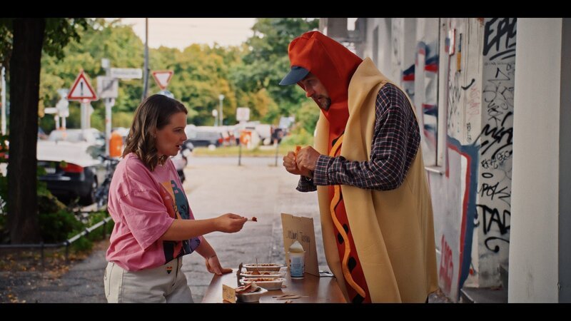 Konnopke (Alexander Finkenwirth) verkauft einer Passantin (Jasna Fritzi Bauer) ein Currywurst-Tasting. – Bild: ZDF und Joseph Strauch