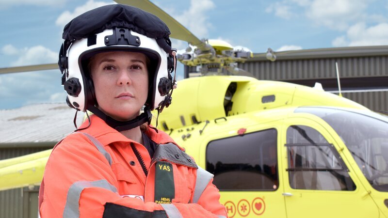 Eine Frau mit Fliegerhelm und orange-schwarzer Uniform vor einem Hubschrauber – Bild: Discovery Communications