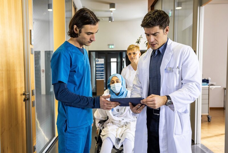 Assistenzarzt Ivo Maric (Jakob D’Aprile, li.) und Oberarzt Dr. Ben Ahlbeck (Philipp Danne, re.) entdecken eine postoperative Komplikation, die bei Filiz Basarni (Tua El-Fawwal, mi. mit Komparse) Schuldgefühle auslöst. – Bild: ARD/​Michael Kremer