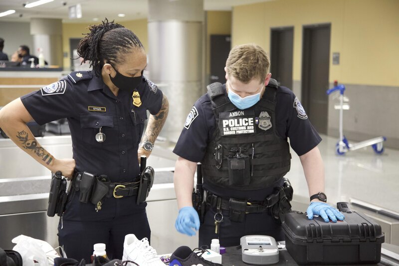 CBP Supervisory Officer Styles (v.l.n.r.) und CBP Officer Axson sehen sich ein Gemini-Gerät an, während sie eine Substanz testen, die im Gepäck eines Passagiers gefunden wurde. (National Geographic) – Bild: 2022 NGC NETWORK US, LLC  All Rights Reserved Lizenzbild frei