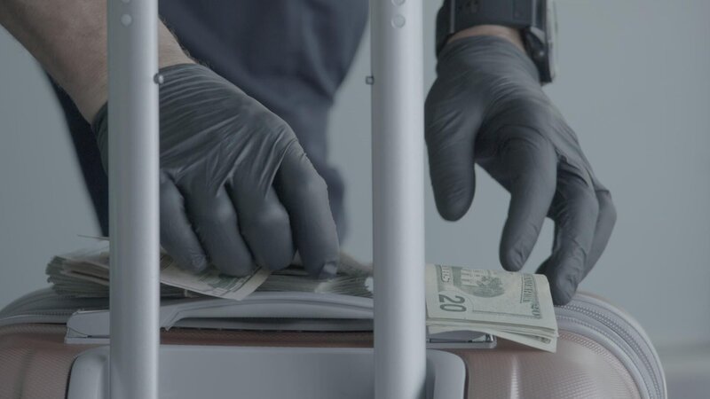 Ein CBP-Beamter zählt das Bargeld eines Passagiers und benutzt das Gepäck des Passagiers als flache Unterlage zum Zählen. (National Geographic) – Bild: 2022 NGC NETWORK US, LLC  All Rights Reserved Lizenzbild frei