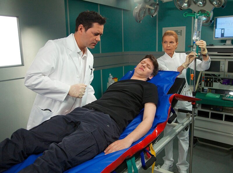 Patrick Janisch wurde bei einem Einbruch von der Hausbesitzerin überrascht und zu Boden geschlagen. Dr. Philipp Brentano stellt bei der Untersuchung eine Wirbelkörperfraktur fest. Patrick muss operiert werden. Als Oberschwester Ingrid Patrick nach Angehörigen fragt, erfahren sie, dass Patricks Mutter vor Kurzem an Krebs gestorben ist, den Vater hat er nie kennengelernt. – Bild: MDR/​Saxonia/​Wernicke