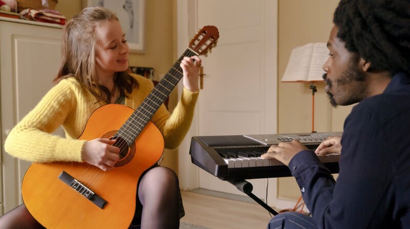 „Tina mobil“ erzählt von den täglichen Problemen und Sorgen einer dreifachen Mutter in Pankow. Julia (Fine Sendel) in ihrem Element: Gitarrenstunde mit ihrem Lehrer Ray (Joel Holmes). – Bild: rbb/​ARD/​X Filme Creative Pool GmbH/​Stefan Erhard