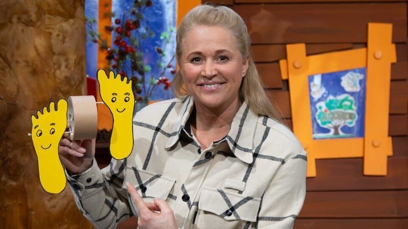 Singa zeigt eine kreative Bastelidee von einer Zuschauerin. Sie zeigt, wie man „Laufende Füße“ bastelt und damit ein lustiges Wettrennen starten kann. – Bild: KiKA