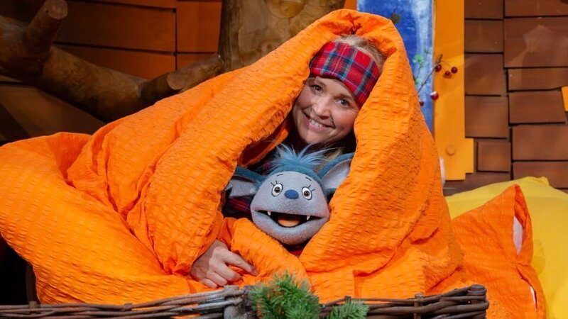 Singa und Fidi spielen Winterschlaf, wie die Tiere im Wald. Sie ziehen sich Schlafsachen an und kuscheln sich unter eine große Decke. – Bild: KiKA