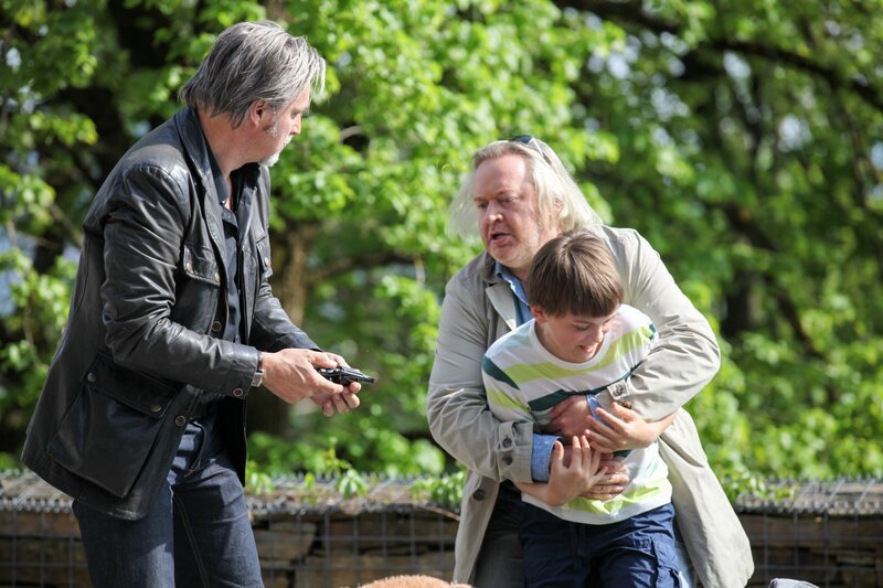 Ribarski (Stefan Jürgens, l.) und Nowak (Gregor Seberg, r.) haben Moritz (Leon Orlandianyi) seine, im Teddy versteckte, Waffe abgenommen und ihn davon abgehalten, auf seine Verwandten zu schießen. – Bild: ORF 1