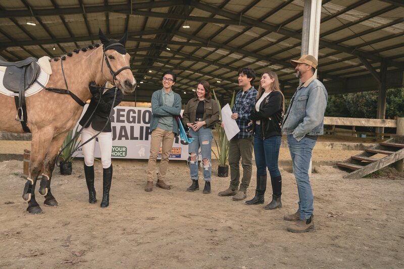 Vor der Qualifikation fürs Regionalteam reden alle – von links: Caleb (Joshua Tan), Issie (Macey Chipping), Dan (Max Crean), Natascha (Antonia Robinson) und Tom (Kirk Torrance) – ihrer Teamkollegin Caroline (Jacqueline Joe), die ihr Pferd startklar macht, gut zu und machen ihr Mut. – Bild: ZDF/​Libertine Pictures Limited/​Slim Film/​ Television Limited