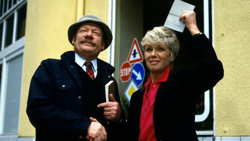 Geschafft – der Fahrprüfer (Wolfgang Völz) gratuliert Hannelore Wichert (Maria Sebaldt) zur bestandenen Führerscheinprüfung. – Bild: Terranova