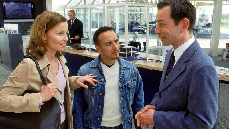 Semir (Erdogan Atalay, Mi.) ist ein wenig verwundert, dass Andrea (Carina Wiese) von dem auf einmal höflichen Autoverkäufer (Anton Figl) problemlos einen Leihwagen bekommt … – Bild: MG RTL D /​ Guido Engels