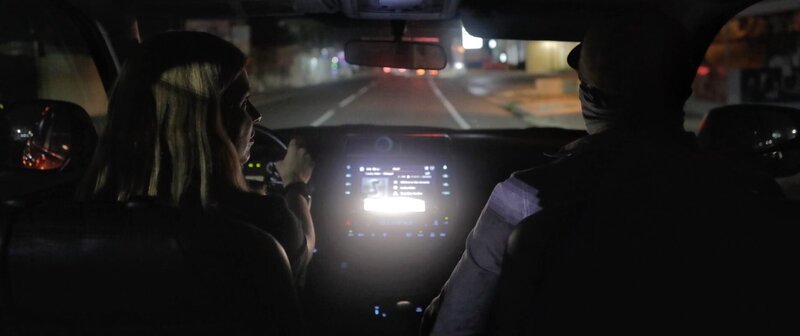 Mariana van Zeller driving with a masked subject inside a car. – Bild: National Geographic