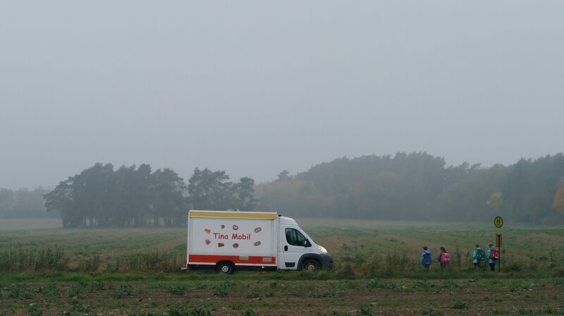 „Tina mobil“ erzählt von den täglichen Problemen und Sorgen einer dreifachen Mutter in Pankow. Der Kampf ums Überleben, das mangelnde Geld – aber Tinas Maxime ist: Man kann alles schaffen, was man will. Und wenn man es nicht schafft, hat man es eben nicht genug gewollt. – Tinas Mobil fährt durchs Morgengrauen. An einer Haltestelle stehen Grundschüler und warten auf den Bus. – Bild: rbb/​ARD/​X Filme Creative Pool GmbH/​Stefan Erhard