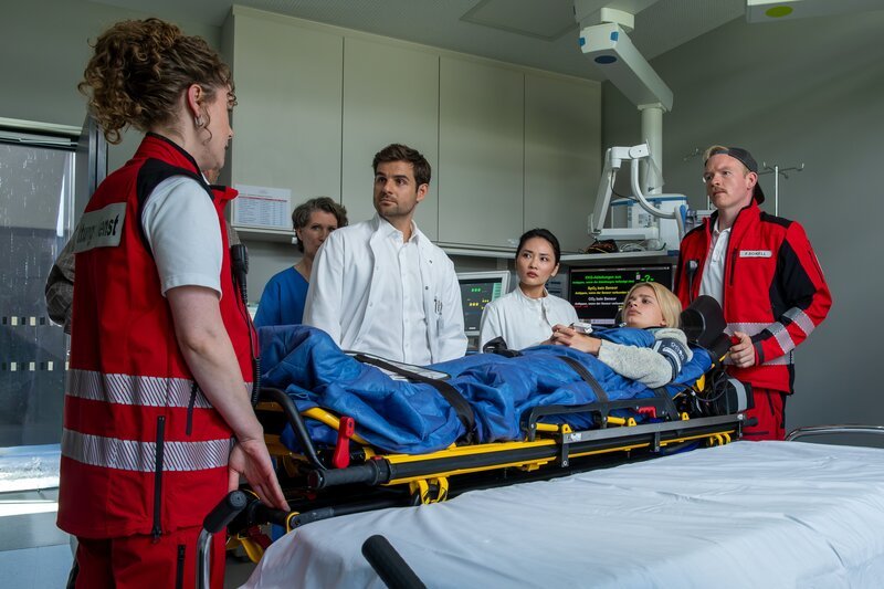 In der Klinik stellt Elli Kempfer (Klara Deutschmann, l.) den bisherigen Befund von Alma Breitner (Renée Gerschke, 2.v.r.) infrage und bringt eine entscheidende Wende, die Dr. Jasper Graf (Lucas Reiber, 3.v.l.), Dr. Mai Trang (Mai Duong Kieu, 3.v.r.) und Felix Sorell (Sebastian Griegel, r.) zunächst überrascht. – Bild: ZDF und Susanne Bernhard
