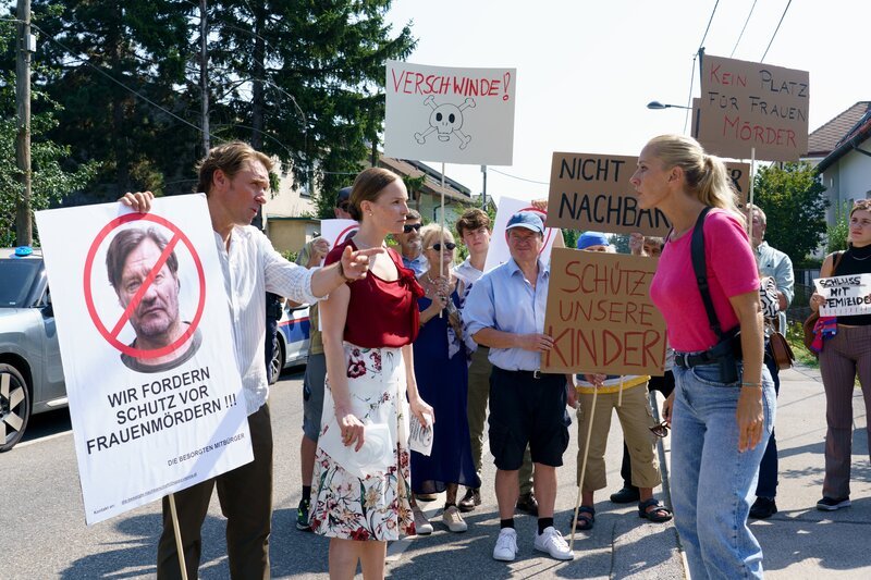 Valentin Exner (Peter Fieseler, l.) und Agnes Exner (Julia Koch, 2.v.l.) und die Nachbarschaft (Komparsen) demonstrieren gegen Gernot Polmer, während Gruppeninspektorin Penny Lanz (Lilian Klebow, 3.v.r.) dies unterbindet. – Bild: Petro Domenigg/​FILMSTILLS.AT KG /​ ZDF