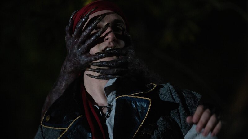 A pair of black demon hands with long nails wraps around the teenage PIRATE’S head in the woods at night. – Bild: Warner Bros. Discovery, Inc.