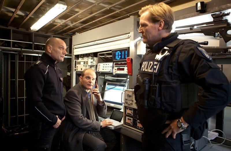 Banküberfall in Berlin-Mitte: Johannes Sonntag (Matthias Klimsa, M.) versucht im Beisein von Jürgen Klug (Torsten Michaelis, l.) und Thomas Kraft (Sascha Gluth, r.) die geforderte Lösegeldsumme zu beschaffen. – Bild: ARD/​Daniela Incoronato
