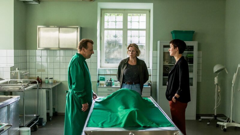 Die Tote vom Seeufer stellt sich als Chefin einer örtlichen Schönheitsklinik heraus. Gerichtsmediziner Gregor Eisen (Ronald Kukulies, l.) hat neue Informationen zum Todesfall für die Ermittlerinnen Doro Beitinger (Franziska Weisz, M.) und Chiara Locatelli (Maria Wördemann, r.). – Bild: ZDF /​ ORF /​ Constantin Campean