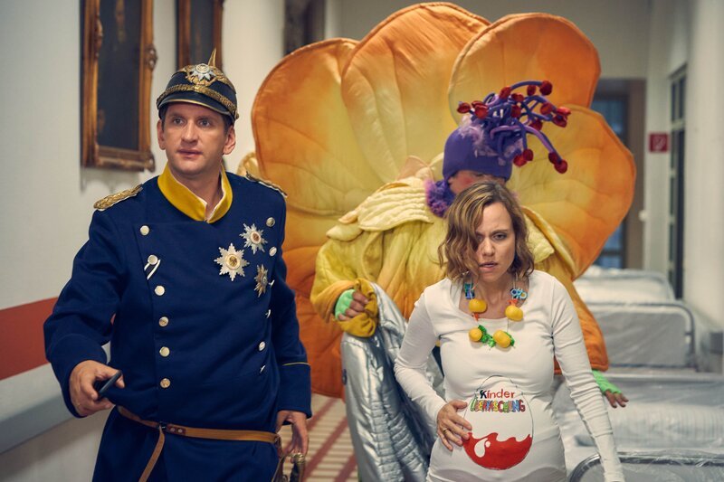Lars (Sebastian Schwarz, l.) und Malte (Daniel Zillmann, 2.v.r.) begleiten Anita (Nadja Becker, r.), deren Wehen mitten im Karneval eingesetzt haben, ins Krankenhaus. – Bild: Frank Dicks