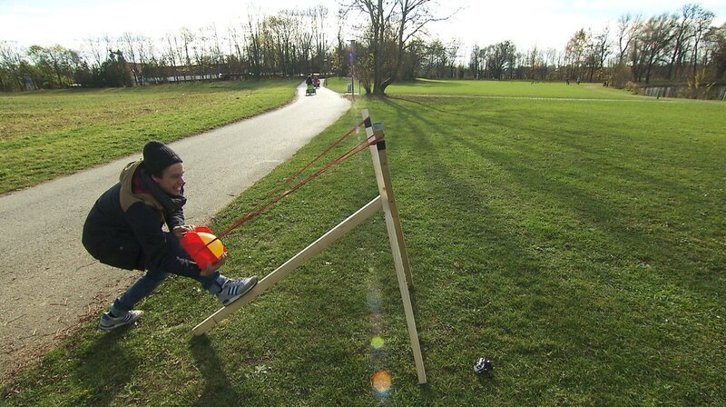 Checker Tobi spannt eine Wasserbombe ins Katapult. – Bild: BR/​megaherz gmbh/​Hans-Florian Hopfner