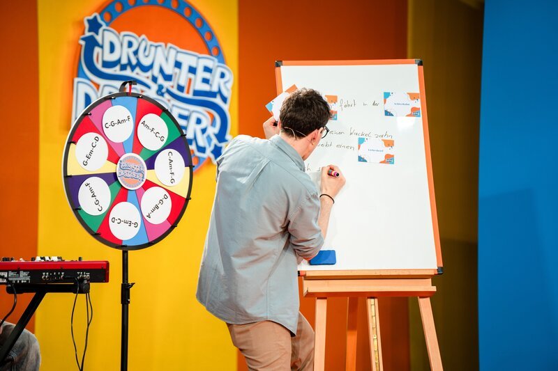 Christoph Hirschler schreibt Liedzeilen auf eine Tafel. – Bild: ORF/​Tambalina Entertainment/​Alex Schwarz Photography