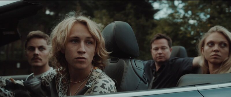 Nasser stellt sich vor, er darf in Schweden einreisen. In seiner Vorstellung fahren da alle Jugendlichen im Cabrio und sind gut drauf. Von links: Ein Schwede (Jonathan Peller), ein schwedischer Fahrer (Anselm Haderer), ein Mitfahrer (Konstantin Krisch) und eine Studentin (Eva Ariane Heise) – Bild: Noaz Deshe/​Arden Film /​ ZDF