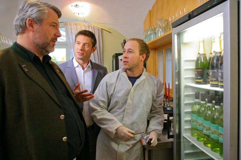 Die Rosenheimer Ermittler Stadler (Dieter Fischer, l.), Hansen (Igor Jefti?, M.) und Högl (Felix Auer, r.) rätseln, was es mit der fehlenden Champagnerflasche auf sich hat. – Bild: ZDF/​Christian A. Rieger – klick