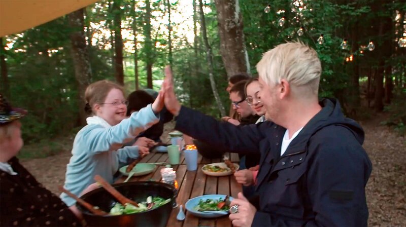 Die Gruppe sitzt nach dem Grillen beim Essen, Rosalie und Ross schlagen ein. – Bild: SWR/​SEO Entertainment
