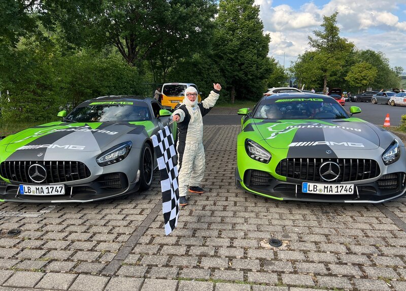 Patrick steht, die Startfahne hissend, zwischen zwei Rennautos. – Bild: SWR/​SEO Entertainment