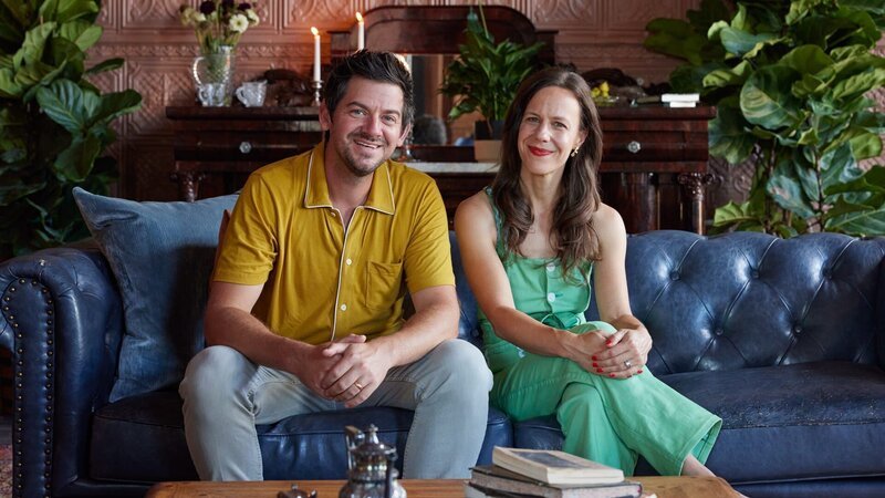 Ethan and Elizabeth Finkelstein sitting on couch in the parlor of the Whitehall firehouse after the renovation, as seen on Who’s Afraid of a Cheap Old House?, Season 1. – Bild: Warner Bros. Discovery, Inc. or its subsidiaries and affiliates