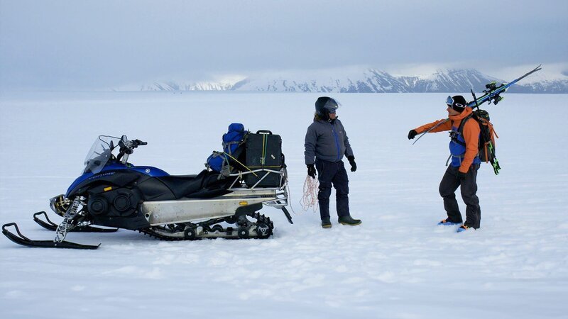 Zwei Personen unterhalten sich in der Nähe von Schneemobilen – Bild: Hip Trips