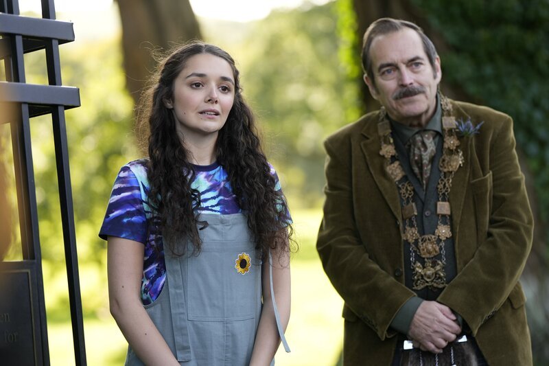 Addie (Lola Blue, links) wird zu ihrem Einsatz für die Hexen-Gedenktafel interviewt. Mr. Macintosh (John Draycott) unterstützt sie. – Bild: ZDF/​Kind Of Productions Limited