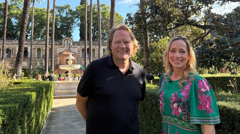 Björn Freitag (l) und Tamina Kallert unterwegs in den malerischen Gärten des Königspalastes Real Alcázar – ein Ort voller Geschichte und andalusischer Pracht. – Bild: WDR/​2bild GmbH/​Lisa Frising