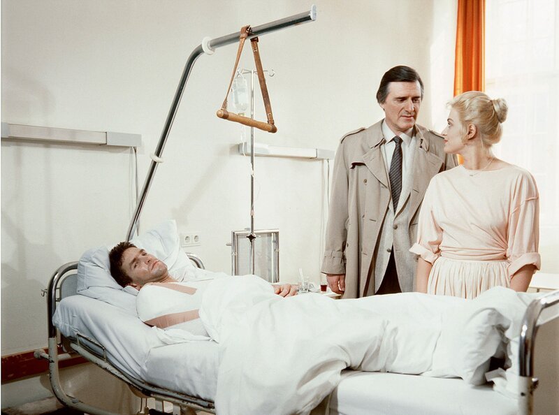 Kriminalkommissar Lenz (Helmut Fischer) mit Petty (Brigitte Obermeier) am Krankenbett des durch eine Kugel schwerverletzten Burt Baxter (William Mang). – Bild: HR/​WDR/​BR