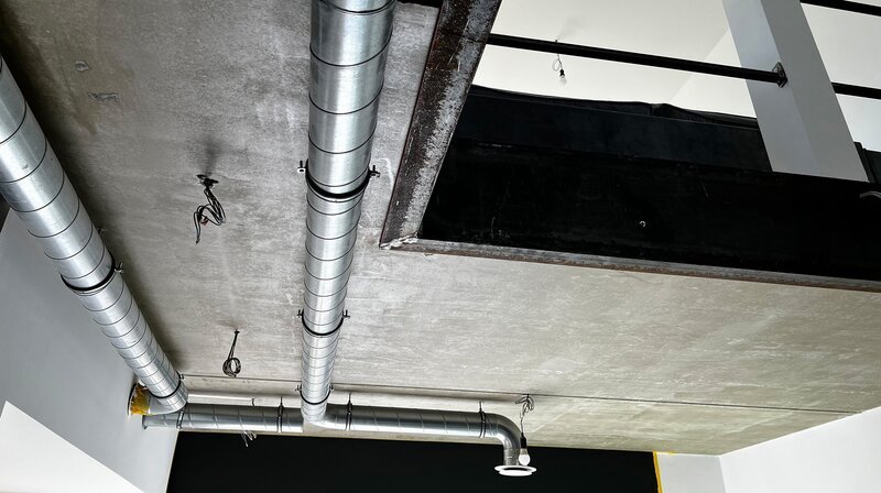 Lüftungsrohre, Eisenträger und rauer Beton prägen das Wohnzimmer. So soll der Charakter des Schlachthauses beibehalten werden. – Bild: NDR/​Rainer Mueller-Delin