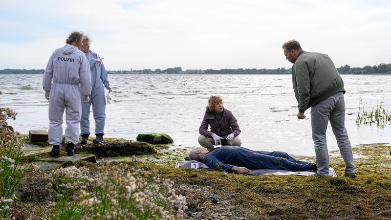 Früh am Morgen entdeckt ein Treibgutsucher eine Wasserleiche. Es handelt sich um Mats Albers (Frank Leal-Soto, 2.v.r.). Dr. Helene Sturbeck (Katharina Blaschke, M.) schließt gegenüber Lars Pöhlmann (Dominic Boeer, r.) einen Mord nicht aus, da der Tote heftige Wunden an den Fingern aufweist. – Bild: ZDF und Meyerbroeker