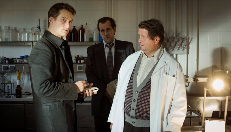 Der Journalist David Burger (Alexander Fehling, li.) sucht gemeinsam mit Eike Barschel (Stephan Schad) ein toxikologisches Institut auf und lassen sich von Professor Brandenburger (Hanspeter Müller-Drossart) eine Theorie erklären, die Selbstmord ausschließt. – Bild: ARD Degeto/​Stephan Rabold