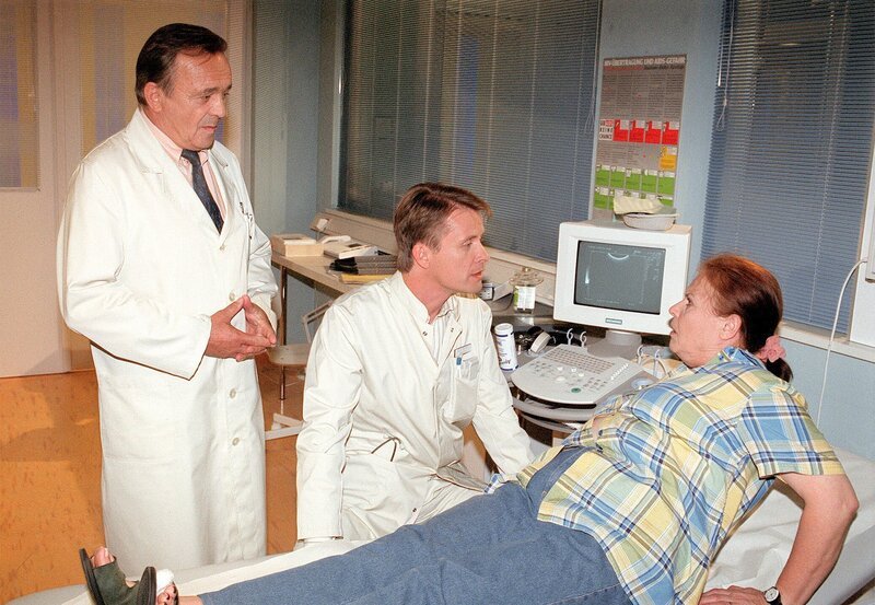 Frau Charlotte hat’s erwischt. Widerwillig liegt sie auf dem Behandlungstisch. Dr. Barach und Prof. Simoni stellen die Diagnose. – Bild: MDR/​Laue