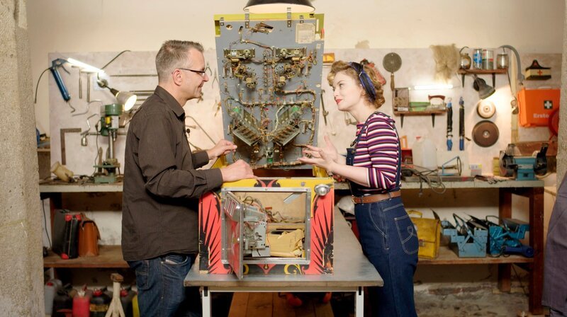 Flipper-Experte Henrick untersucht zusammen mit Victoria Beyer das Innenleben des alten Flippers. – Bild: WDR/​Encanto Film- und Fernsehproduktions GmbH