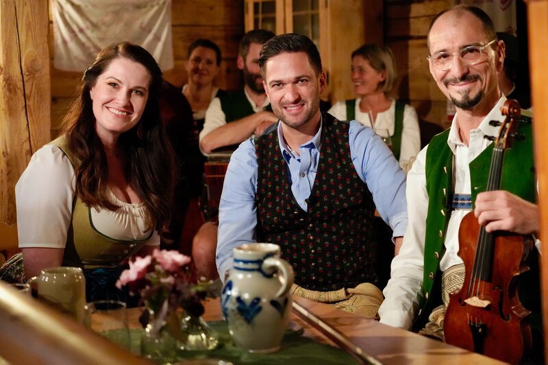 Die ServusTV Moderatoren Conny Bürgler und Richard Deutinger posieren für ein Foto mit Martin Kiesenhofer (rechts) von der Geigenmusi Kiesenhofer, in der Mostschänke Hussenbauer. – Bild: ServusTV /​ Brigitte Erhart /​ Degn Film