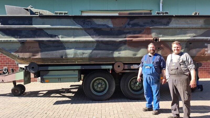 Marcus Thiel and neighbor Stefan Tonne stand in front of the Bundeswehr’s decommissioned M3 boat on the grounds of Thiel Baumschinen in Neerstedt. – Bild: Warner Bros. Discovery, Inc. or its subsidiaries and affiliates /​ Berit Hinnerks