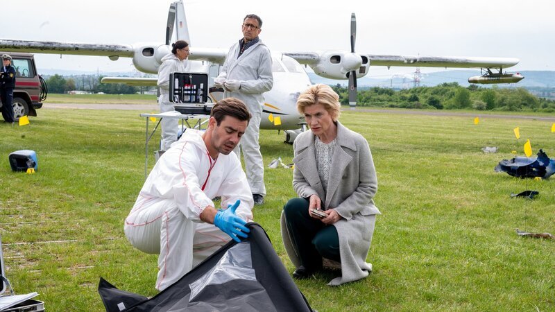 Der Hagelflieger-Pilot Hannes Rieger wird tot aufgefunden. KTU-Leiter Jan Arnaud (Mike Zaka Sommerfeldt, 2.v.r.) und Rechtsmediziner Dr. Benedikt Förster (Florian Wünsche, 2.v.l.) teilen mit der Ersten Kriminalhauptkommissarin Martina Seiffert (Astrid M. Fünderich, r.) ihren Ermittlungsstand: Jemand hat den Piloten erschlagen und versucht, die Tat mit einer fingierten Explosion zu vertuschen. – Bild: ZDF und MARKUS_FENCHEL