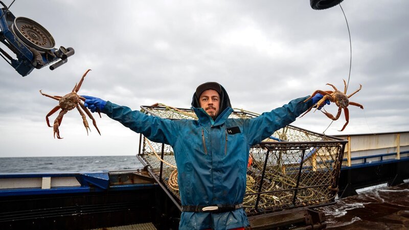 Northwestern deckhand Karl Rasmussen posing holding baridi crab, pot in the background – Bild: Warner Bros. Discovery, Inc. or its subsidiaries and affiliates. All rights reserved.