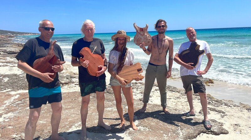 Instrumenten-Taufe im Mittelmeer: Das Werfen des Holzkörpers in die Fluten ist Pflicht im Kurs von Ekki Hoffmann. Nur so kommt der Balearen-Sound in die Gitarre, sagt Ekki (2.v.l.). – Bild: NDR/​Steffen Schneider
